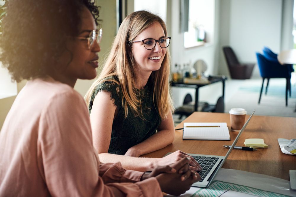 Two happy female colleagues smiling while listening during a meeting