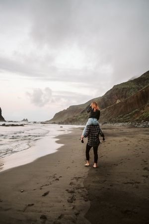 Unrecognizable man carrying woman on shoulders near sea