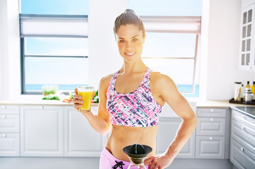 Fit woman posing in kitchen with orange juice and hand on hip