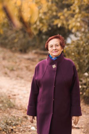 Older woman in purple coat standing near yellow trees