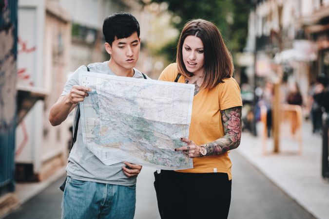 Joyful multiracial tourists checking map and standing on urban street