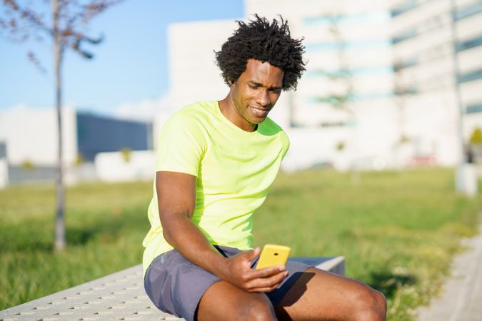 Man sitting on bright day after workout checking phone