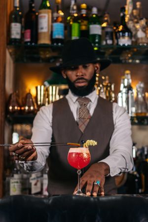 stylish Black bartender offering a customer a cocktail decorated with garnish in a traditional cocktail bar