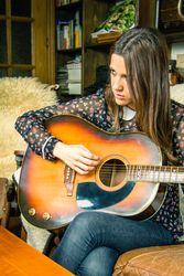 Young hipster woman playing acoustic guitar at home