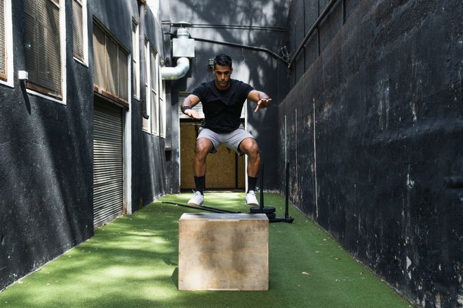 Concentrated athlete jumping on wooden box