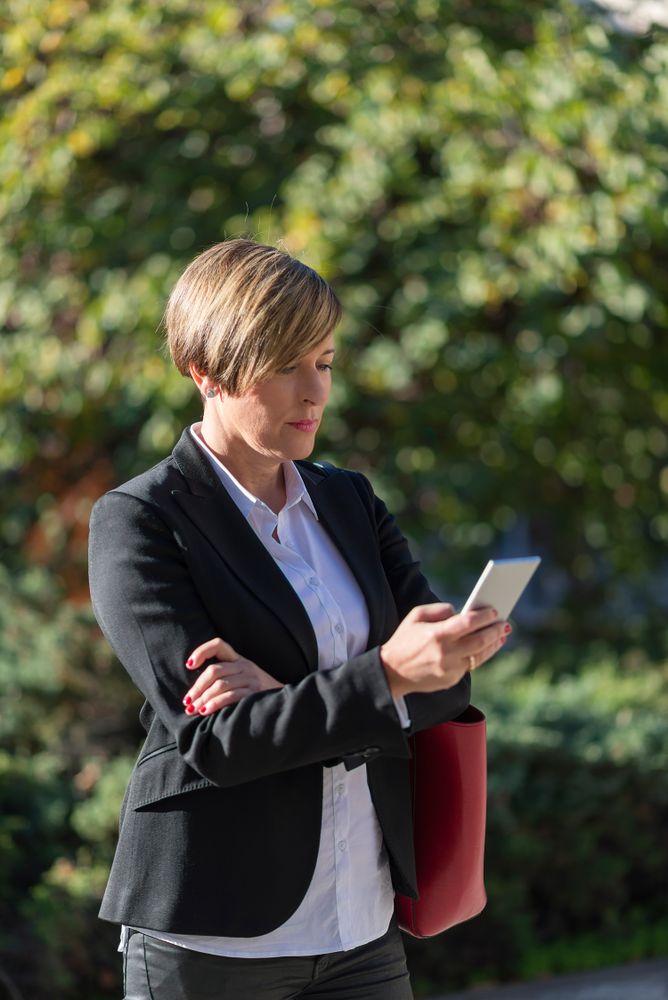 Businesswoman looking at phone in front of hedge