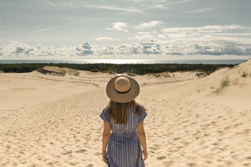 adult woman in casual dress and straw hat standing having good time on sand dune