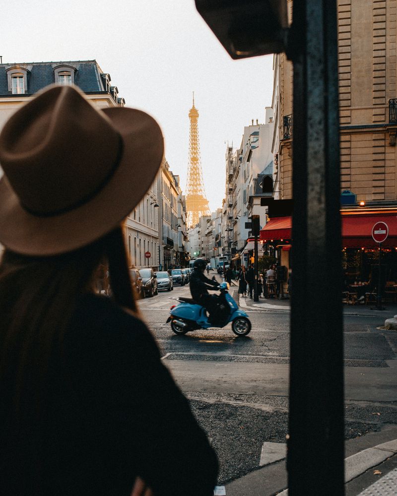 Woman in brown cowboy hat standing on sidewalk near man riding motorcycle on road