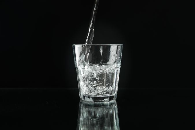 Glass of water being poured in dark room, copy space
