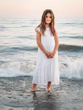 Smiling girl standing on seaside among waves