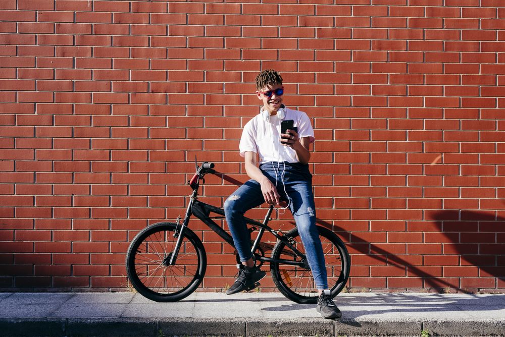 Young happy Black male browsing smartphone on bike