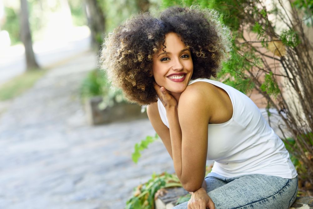 Young Black woman with afro hairstyle smiling while sitting outside, copy space
