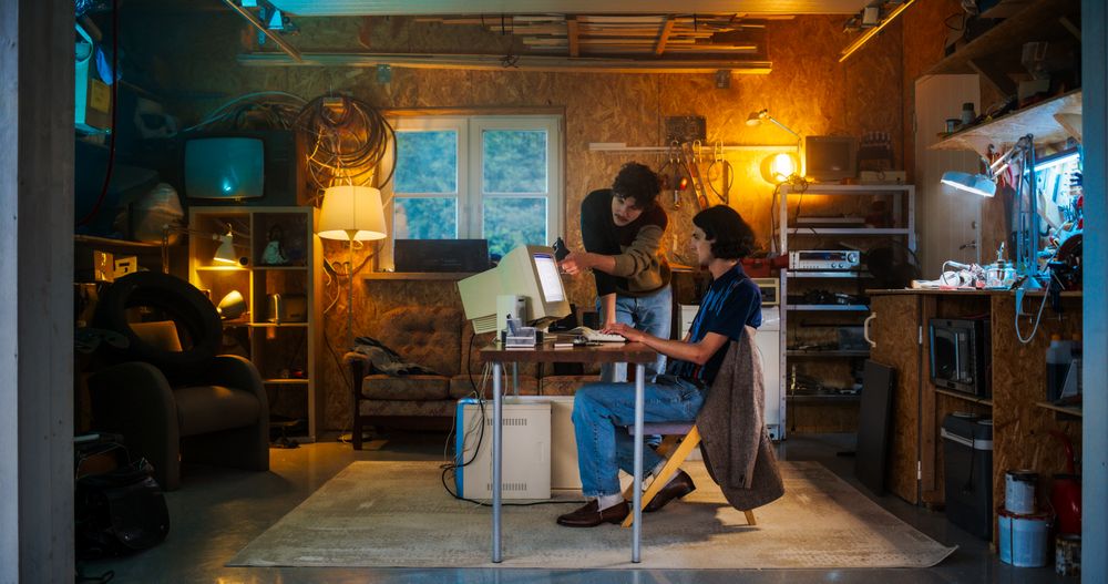 Two Male Tech Startup Founders Using Old Desktop Computer In Retro Garage In The Evening.