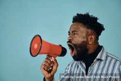 Portrait of a Black man in blue studio shoot screaming into megaphone 4mx8W5