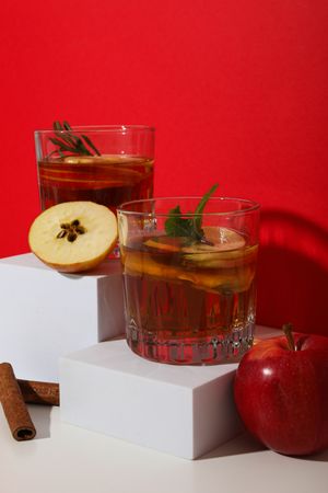 Glasses with apple cider, apples and cinnamon sticks on red background