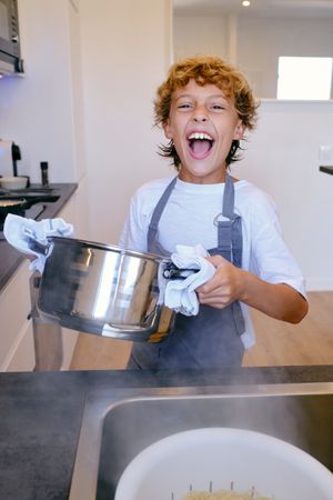 Excited boy with saucepan cooking in kitchen