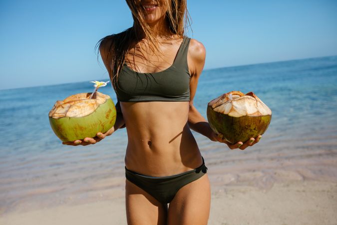 Woman in bikini on the beach with fresh coconuts