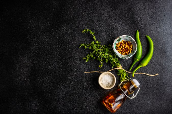 Cooking concept with pepper, herbs, oil and seasoning on dark counter with copy space