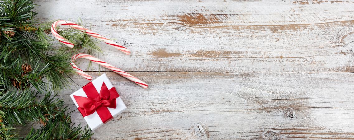 Christmas gift box with border of fir branches and candy canes on rustic wooden background