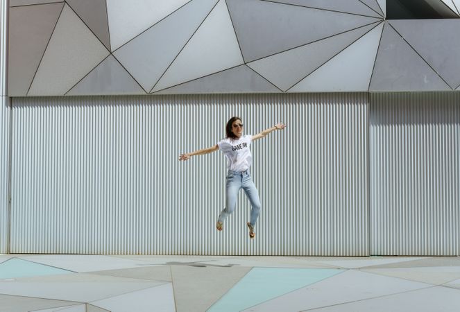 Cheerful woman jumping near modern wall