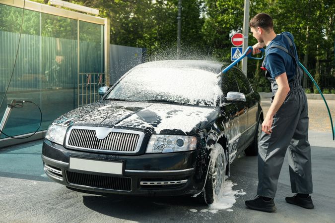 A man washes a car in a manual car wash. Clear car