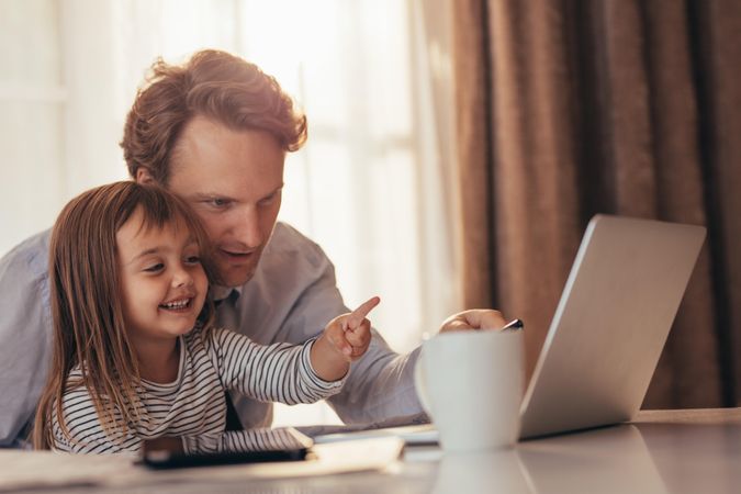 Father working at home with daughter sitting on his lap
