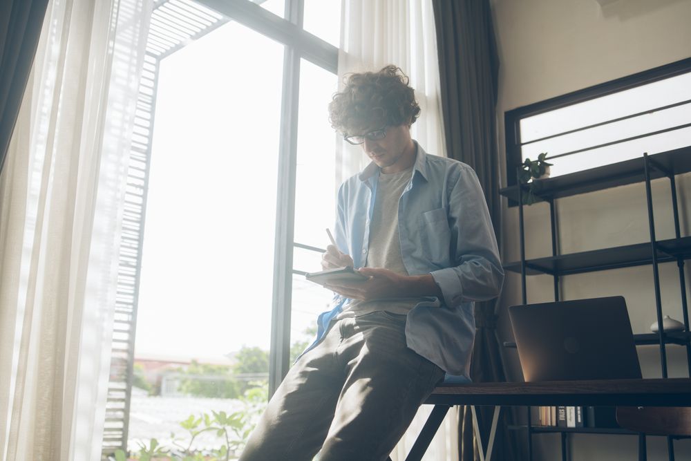 Man writing on tablet while casually sitting on desk at home