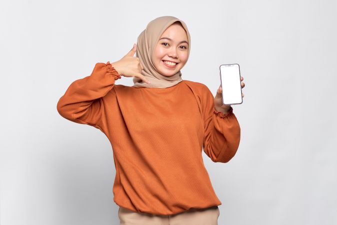 Confident Muslim woman smiling while holding up smart phone screen making call me gesture with hand