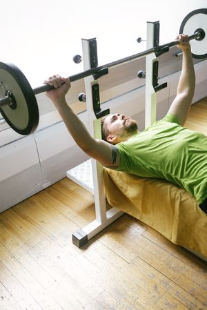 Looking at down at man in green t-shirt lifting heavy bar exercising chest