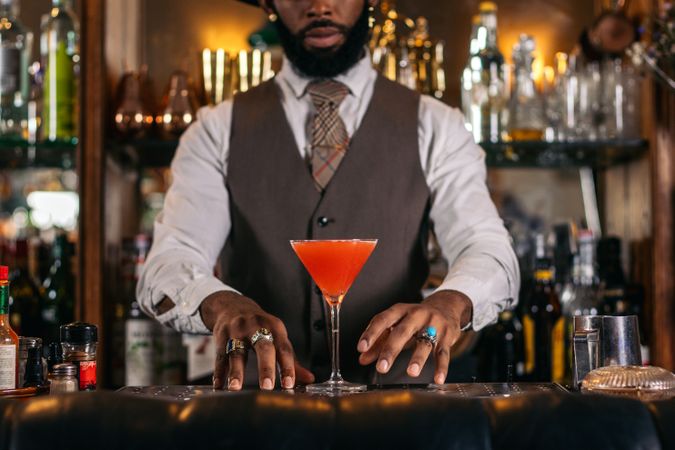 Cutout of a Black bartender offering a cocktail served in a martini glass in a traditional cocktail bar