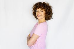 Smiling female in light pink t-shirt standing with arms crossed in blank space