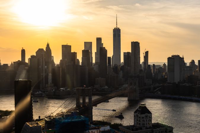 Iconic New York City Landscape Over East River with Skyscrapers, Brooklyn Bridge, Cars and Ferry Boats. Cinematic Evening Urban Skyline with Sunset and Lightly Clouded Sky