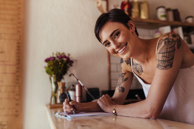 Smiling woman at the counter of her cafe with a pen and pad