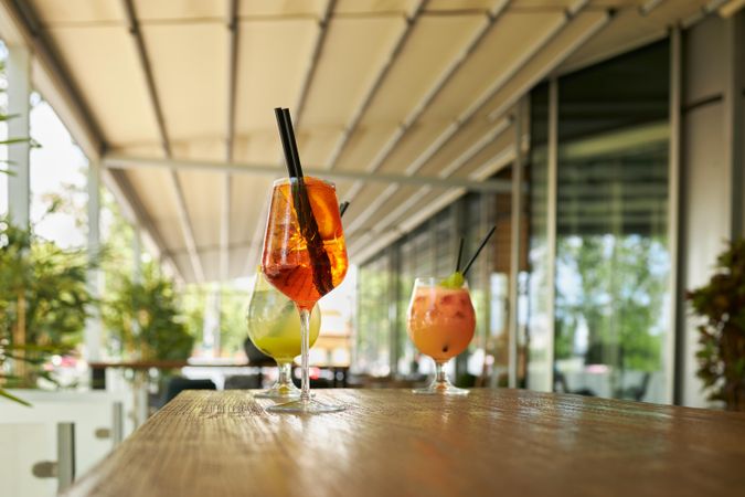 Side view of three colorful cocktails on a wooden table outside
