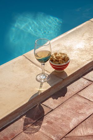 Glass of wine and a bowl of peanuts for an aperitivo by the pool in summer