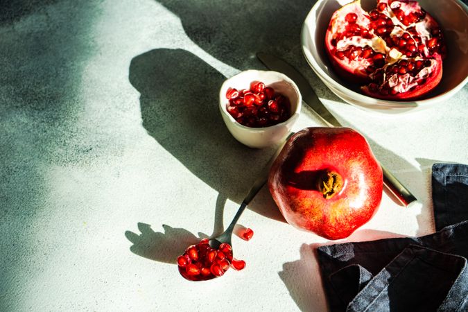 Shadowy table with pomegranate in bowl with side of seeds and spoon