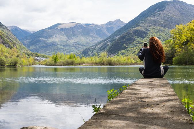 Anonymous traveler taking photo of lake in mountains
