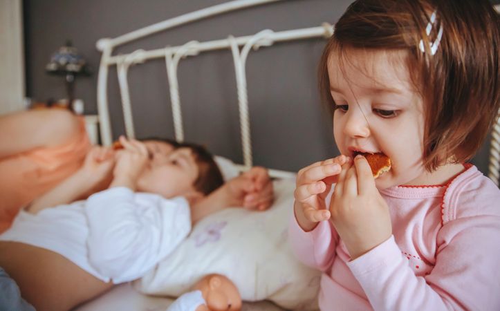 Girl eating cookies in bed next to her mother and brother