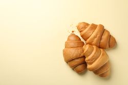 Three baked croissants on beige background, top view with copy space
