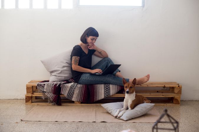 Woman on wooden bench working from home on laptop with dog at her feet