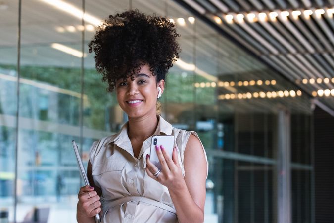 Smiling Black pregnant woman using smartphone and wireless earphones