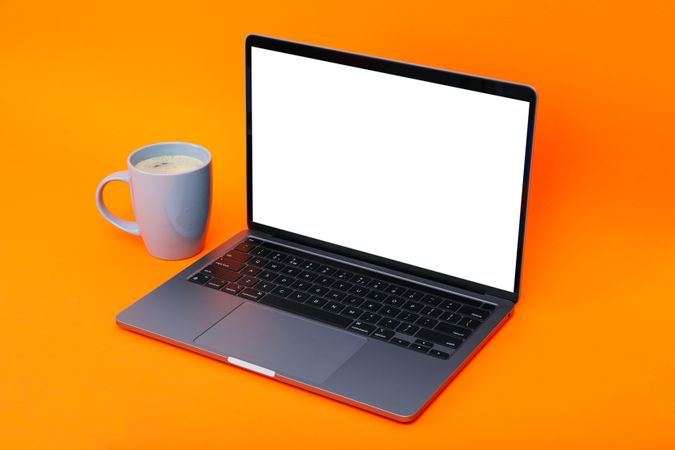 Laptop at angle with mockup screen with cup of coffee or tea in orange studio shoot