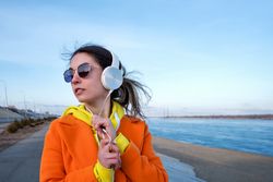 Cool woman in colorful clothes wearing headphones on the coast