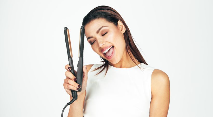Woman with eyes closed holding a hair straightener close to her head