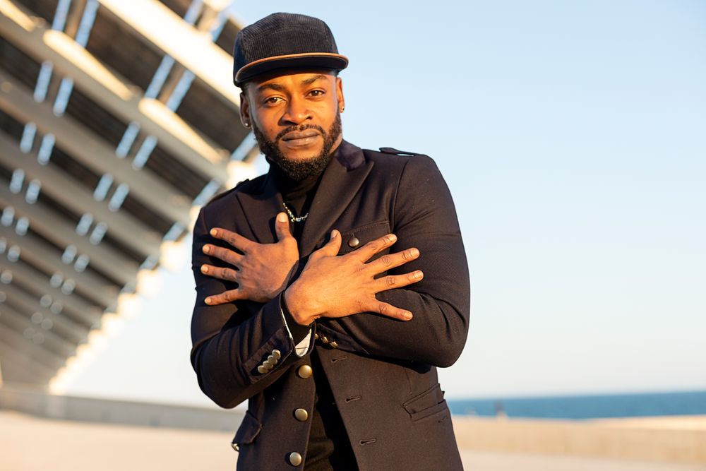 Portrait of stylish Black man standing outdoors in front of modern structure with hands crossed over chest