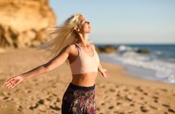 Blonde female with arms out to the ocean on beach