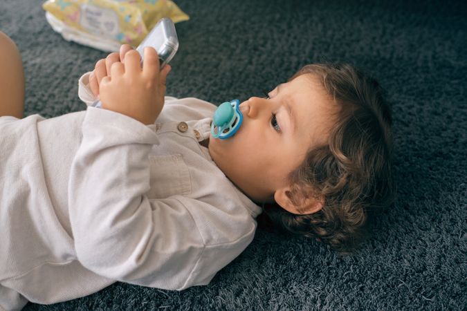 Toddler lying on soft carpet and browsing cellphone