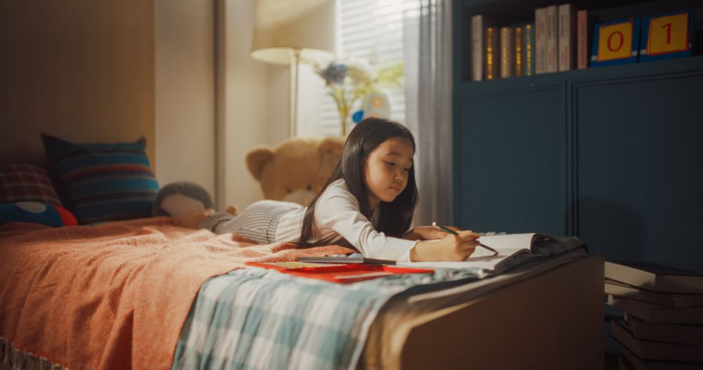 Young Child Lying on a Bed, Using Different Pencils to Make an Artistic Piece for Her Parents