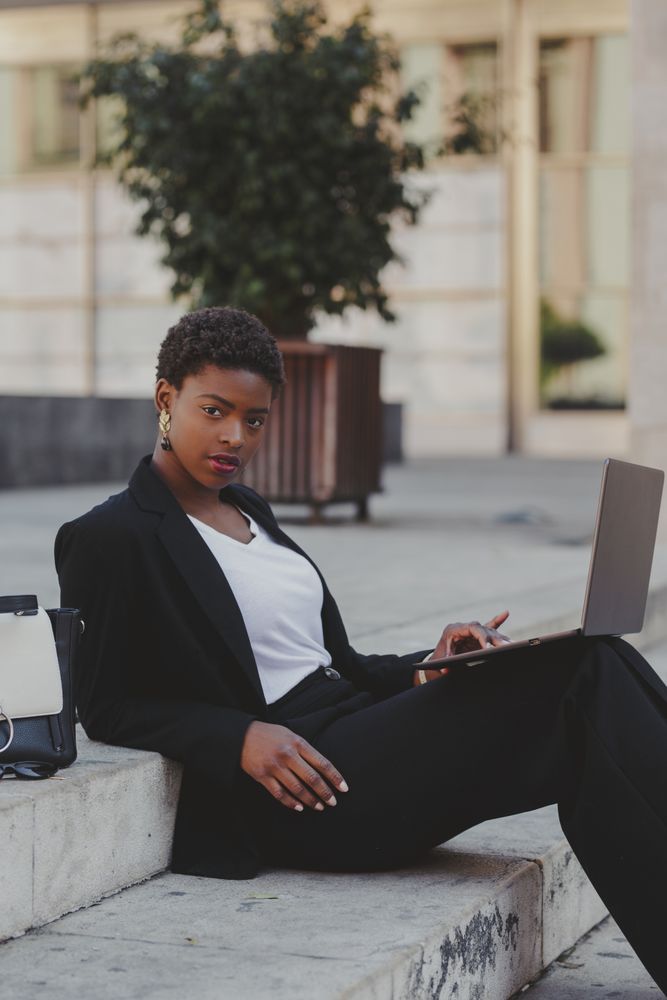 Stylish Black woman with laptop on steps near handbag