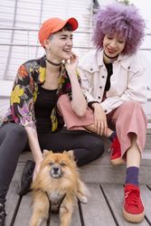 Women in colorful shirt and with pink hair training dog and having fun